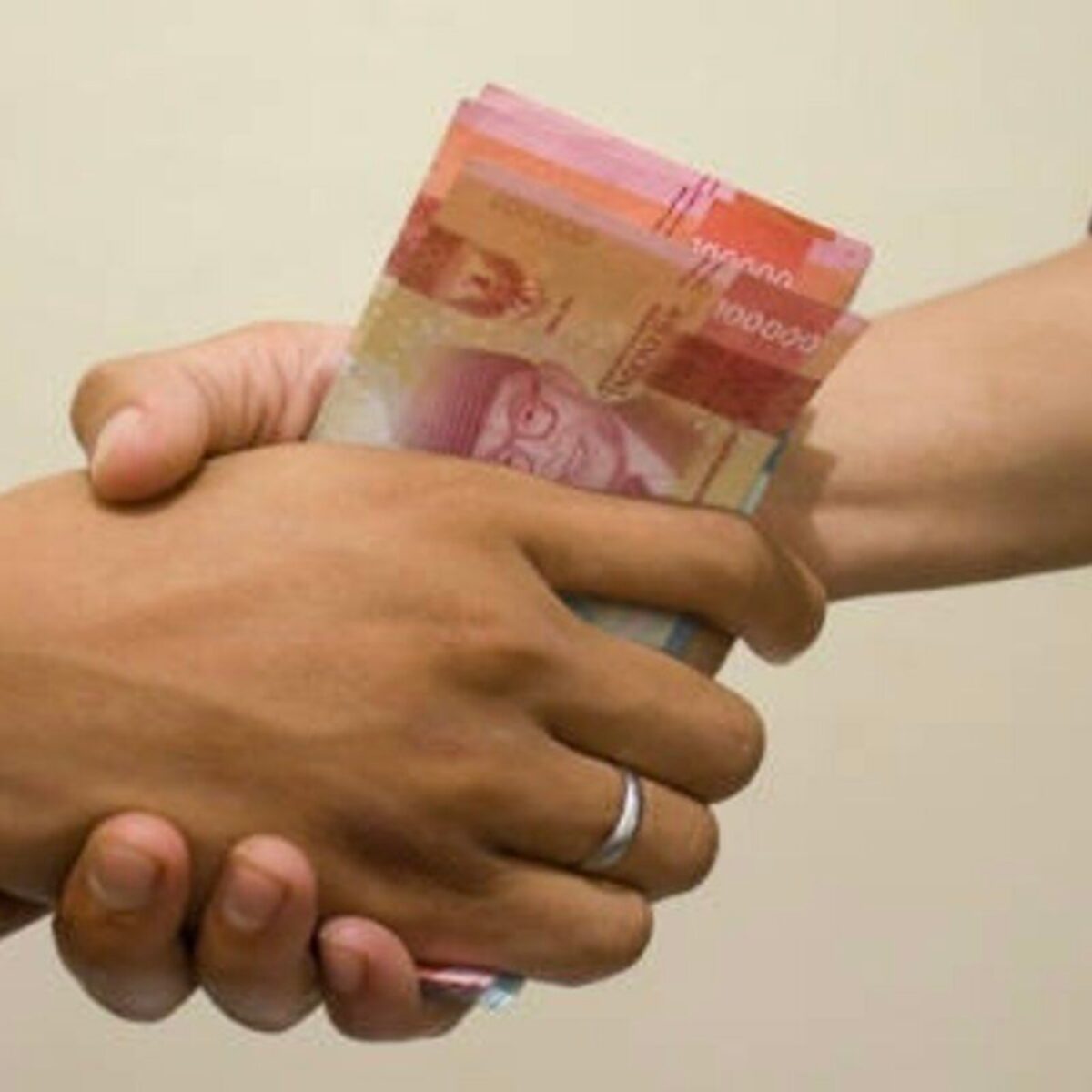 hand is giving bribe. money handshake.  man shaking hands after agreeing deal with indonesian rupiah on brown background