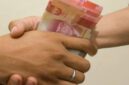 hand is giving bribe. money handshake.  man shaking hands after agreeing deal with indonesian rupiah on brown background