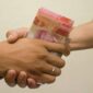 hand is giving bribe. money handshake.  man shaking hands after agreeing deal with indonesian rupiah on brown background